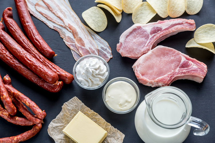 Meats and dairy on a black table including bacon, sausage, milk, chips, and butter