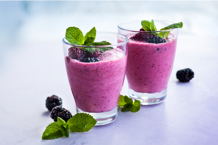 two glasses of tropical berry hibiscus smoothie garnished with blackberry and mint leaves