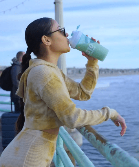 A woman in a yellow tie-dye workout outfit drinks from a 310 shaker bottle.