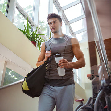 A man in a gym attire with his gym bag while holding his hydration bottle.