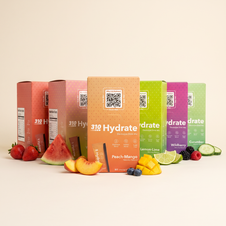 All six 310 Hydrate 15-count flavors with fresh fruit and a splashing glass of water