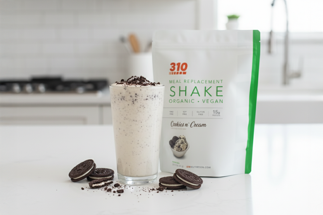Cookies and cream protein shake in a glass topped with crumbs, beside 310 Shake pouch and cookies.