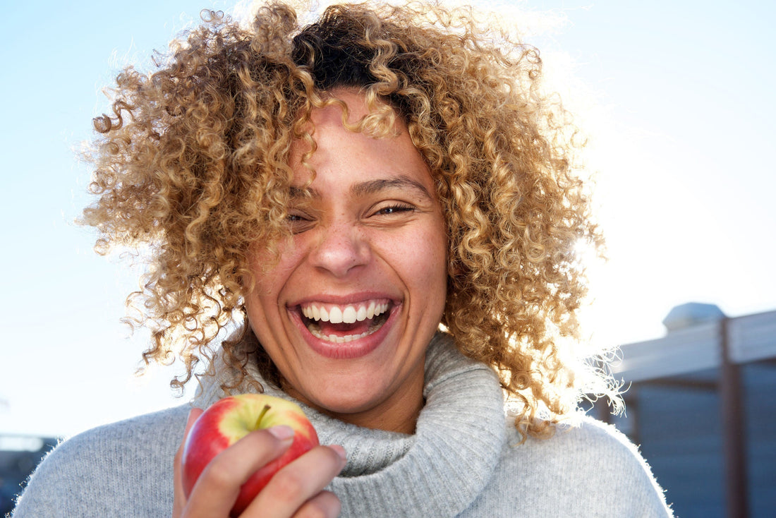 a curly woman smiling while holding an apple