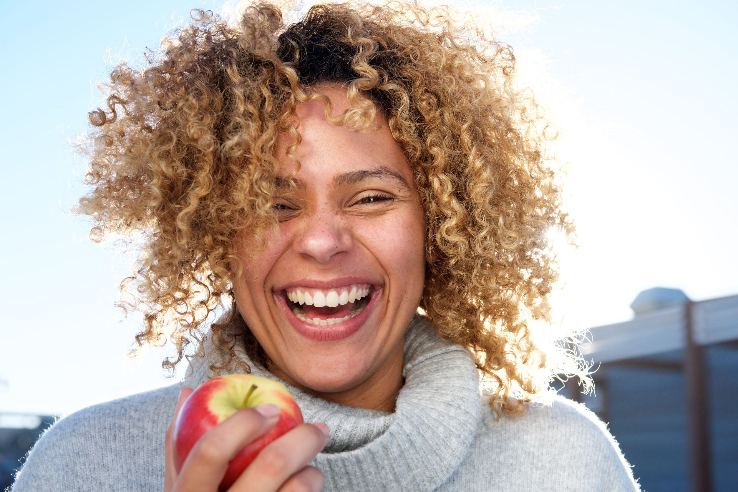 a curly woman smiling while holding an apple