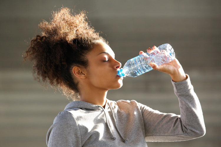 a woman wearing jacket drinking water from a bottled water