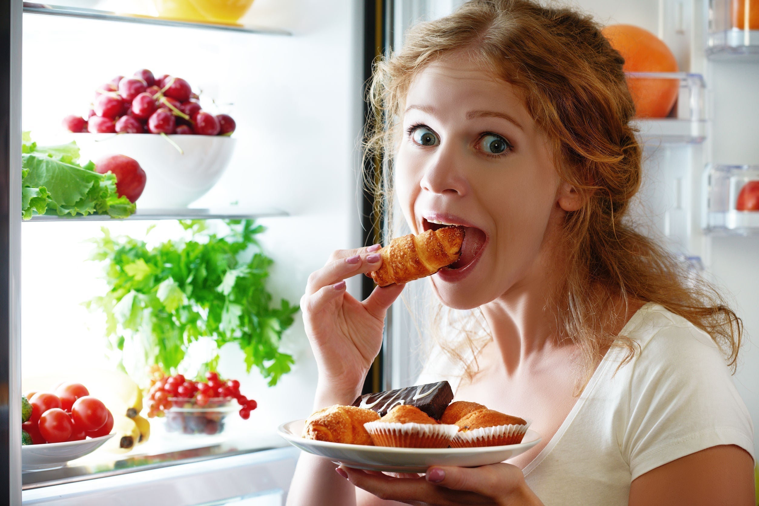 a girl eating dessert with open fridge