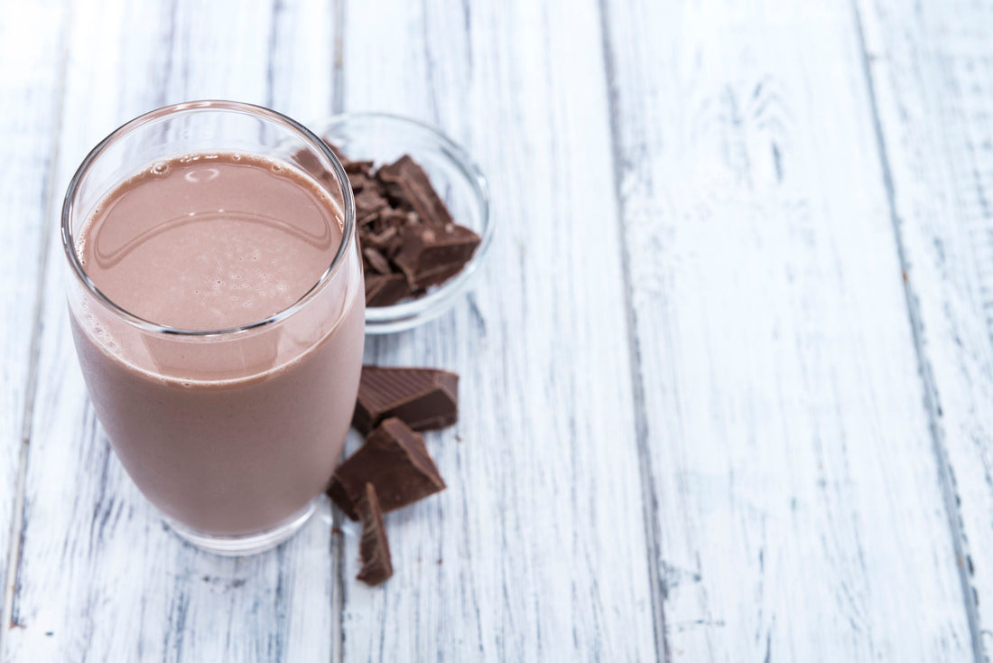 a glass of chocolate shake beside chocolates in a wooden surface