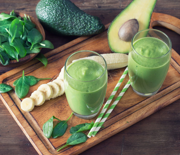 avocado spinach and banana smoothie on wooden cutting board with straws