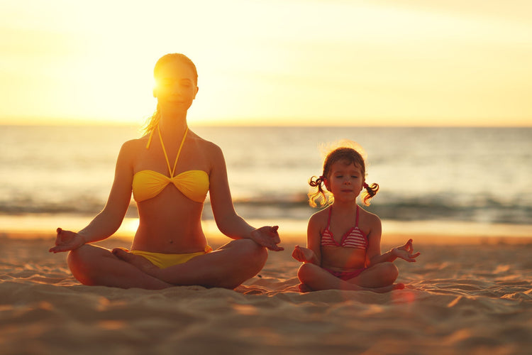 mother and daughter doing yoga at the seashore