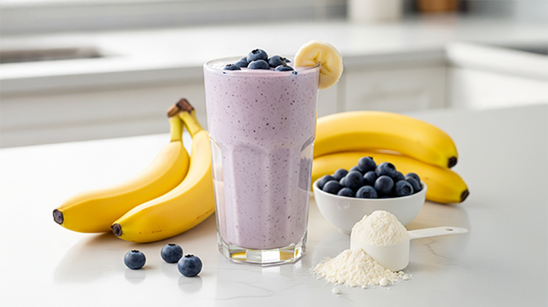 Blueberry banana protein shake topped with blueberries, surrounded by bananas, berries, and powder.
