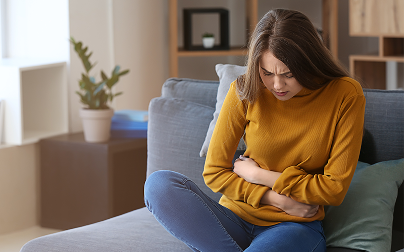 woman sitting on the couch experiencing abdominal pain 