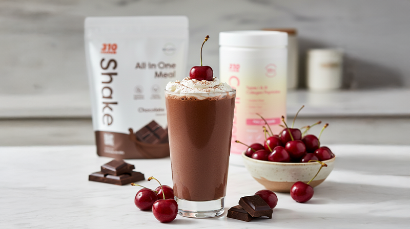 Chocolate shake with whipped cream and cherry on top, surrounded by cherries and chocolate pieces.