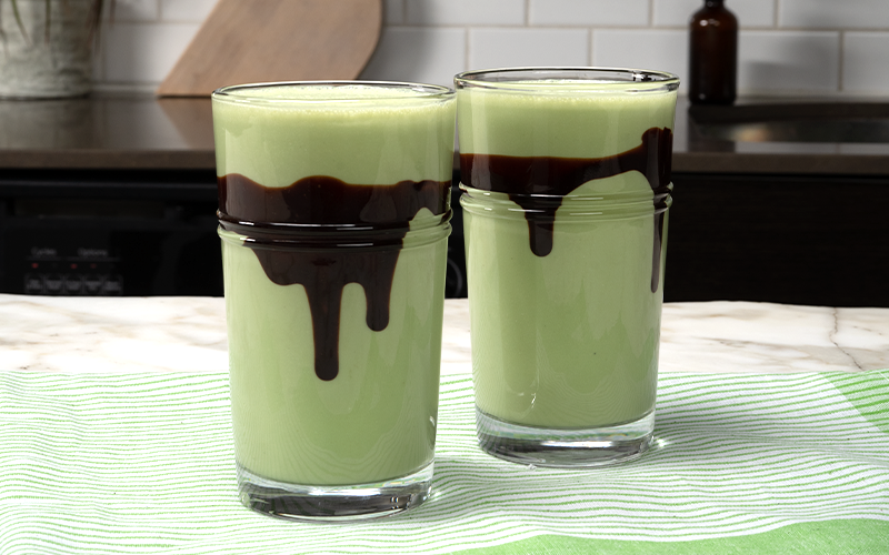 Chocolate smoothie or milkshake with mint and straw, in mason jar on light blue background