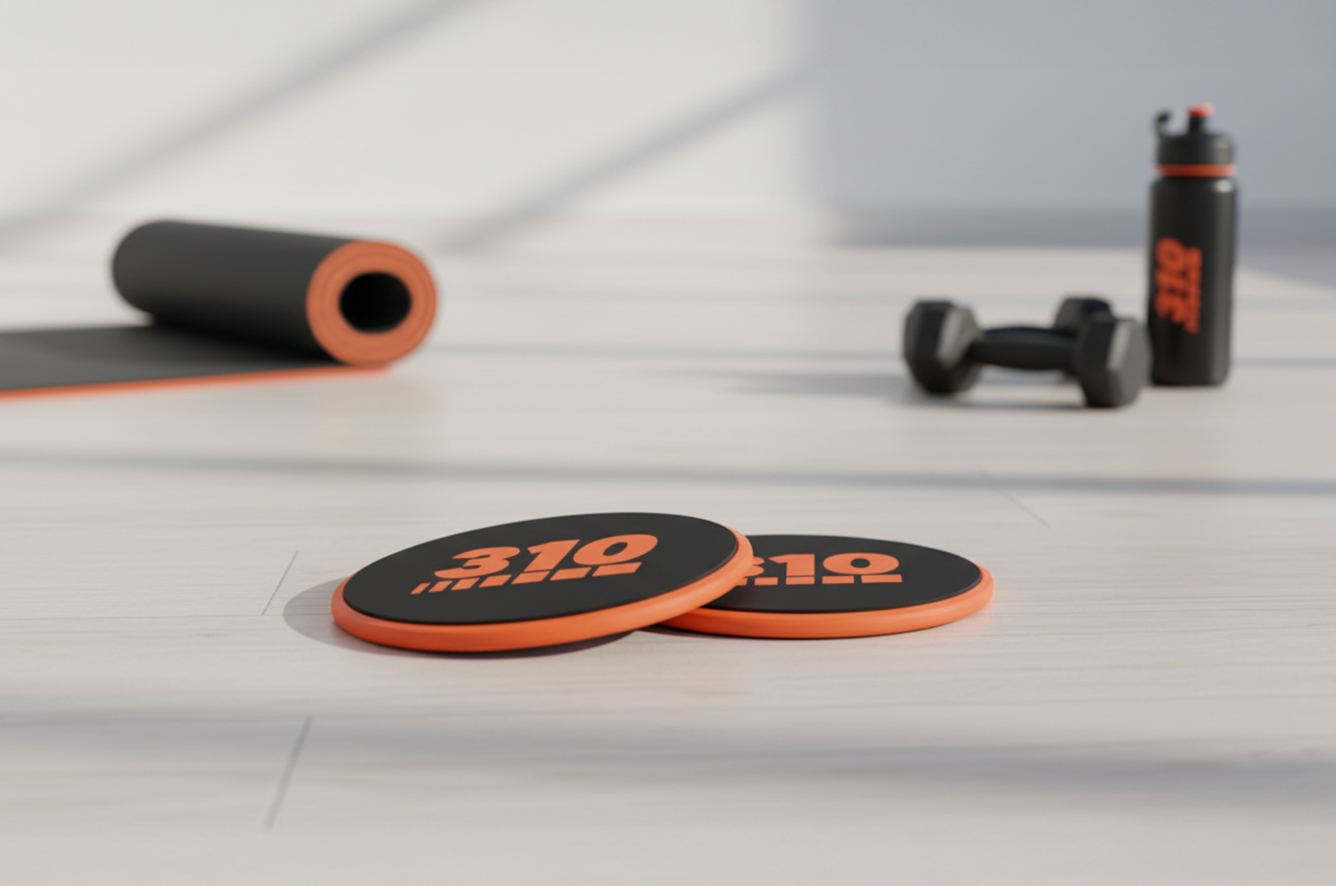 310 exercise sliders on a workout floor with yoga mat, dumbbell, and water bottle in background.