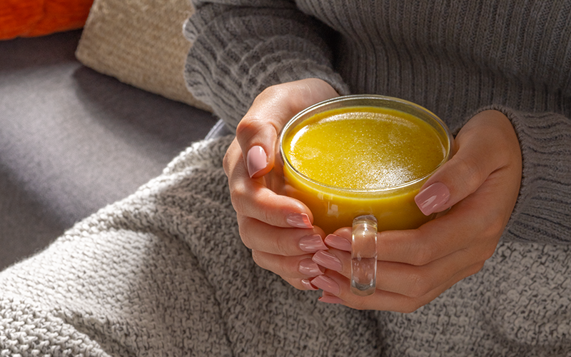 a woman holding a clear glass with turmeric juice