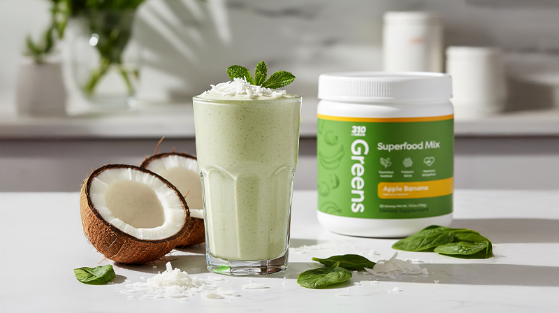 Green coconut smoothie with shredded coconut topping, beside spinach leaves, fresh coconut, and mix.