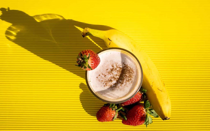 Banana meal replacement shake with strawberries on yellow background.