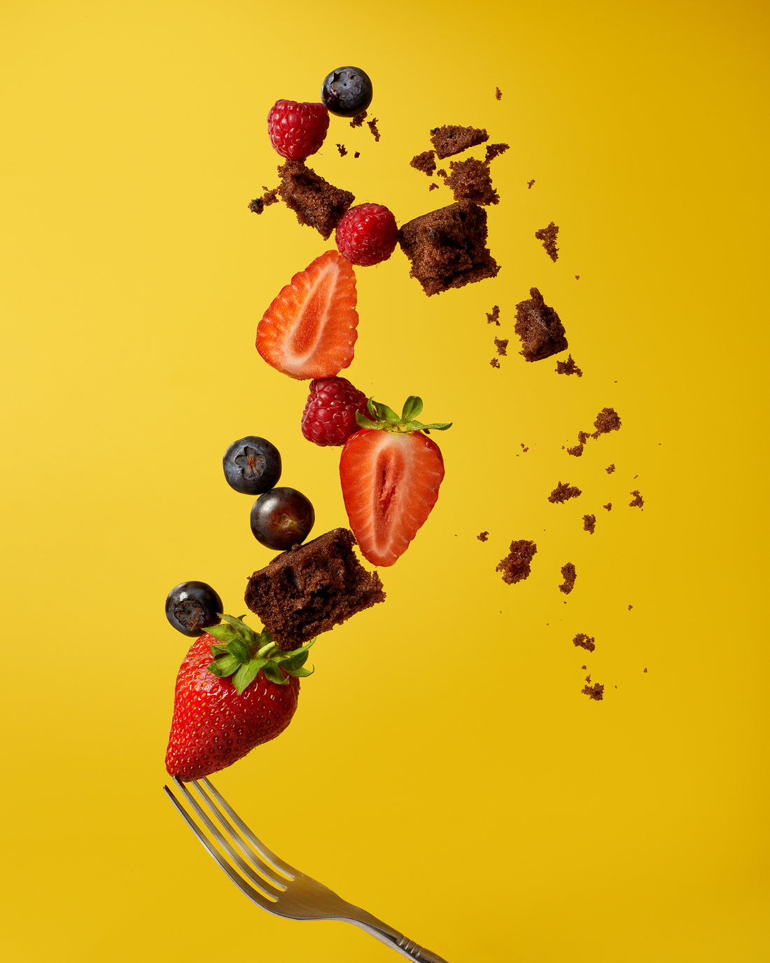 fork, berries and chocolates against a yellow background