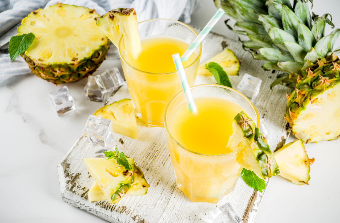 Fresh pineapple juice or cocktail, with pieces of fresh pineapple, ice, decorated with mint, on a white marble table, copy space