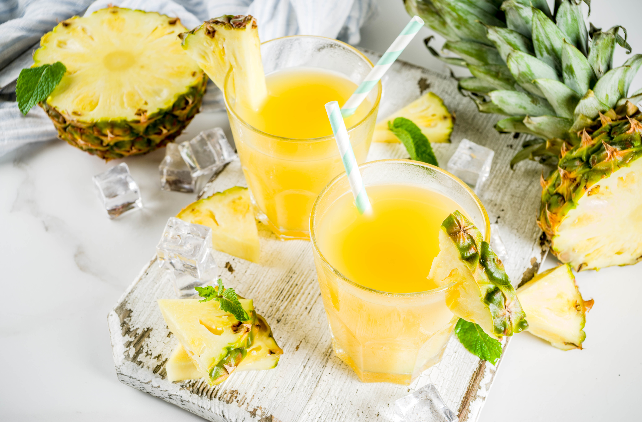 Fresh pineapple juice or cocktail, with pieces of fresh pineapple, ice, decorated with mint, on a white marble table, copy space