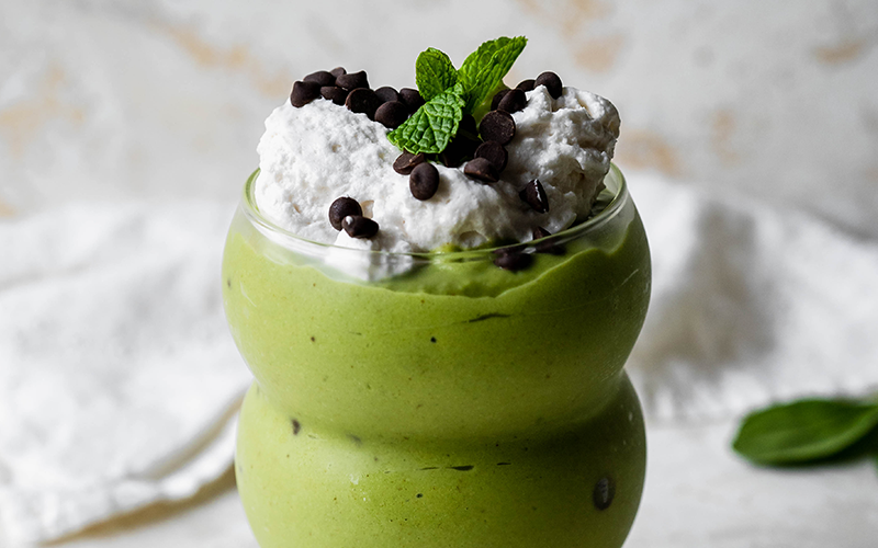 shamrock smoothie topped with whipped cream. chocolate chips and mint leaves