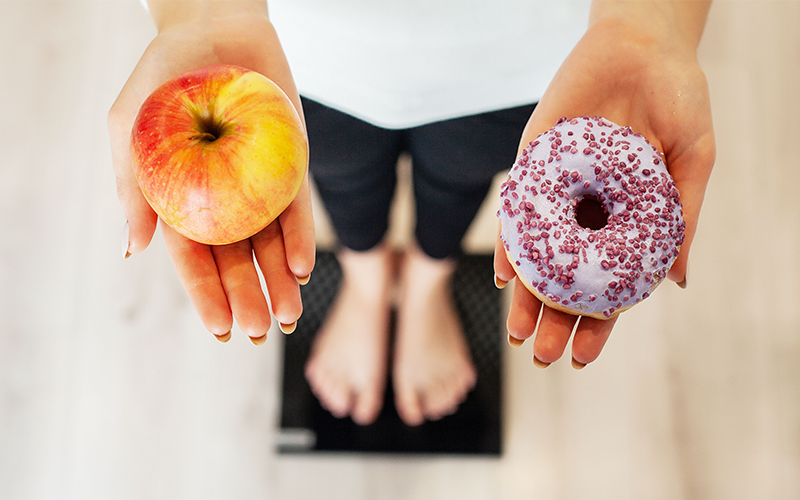 apple and donut on a woman's hand while standing on a digital scale