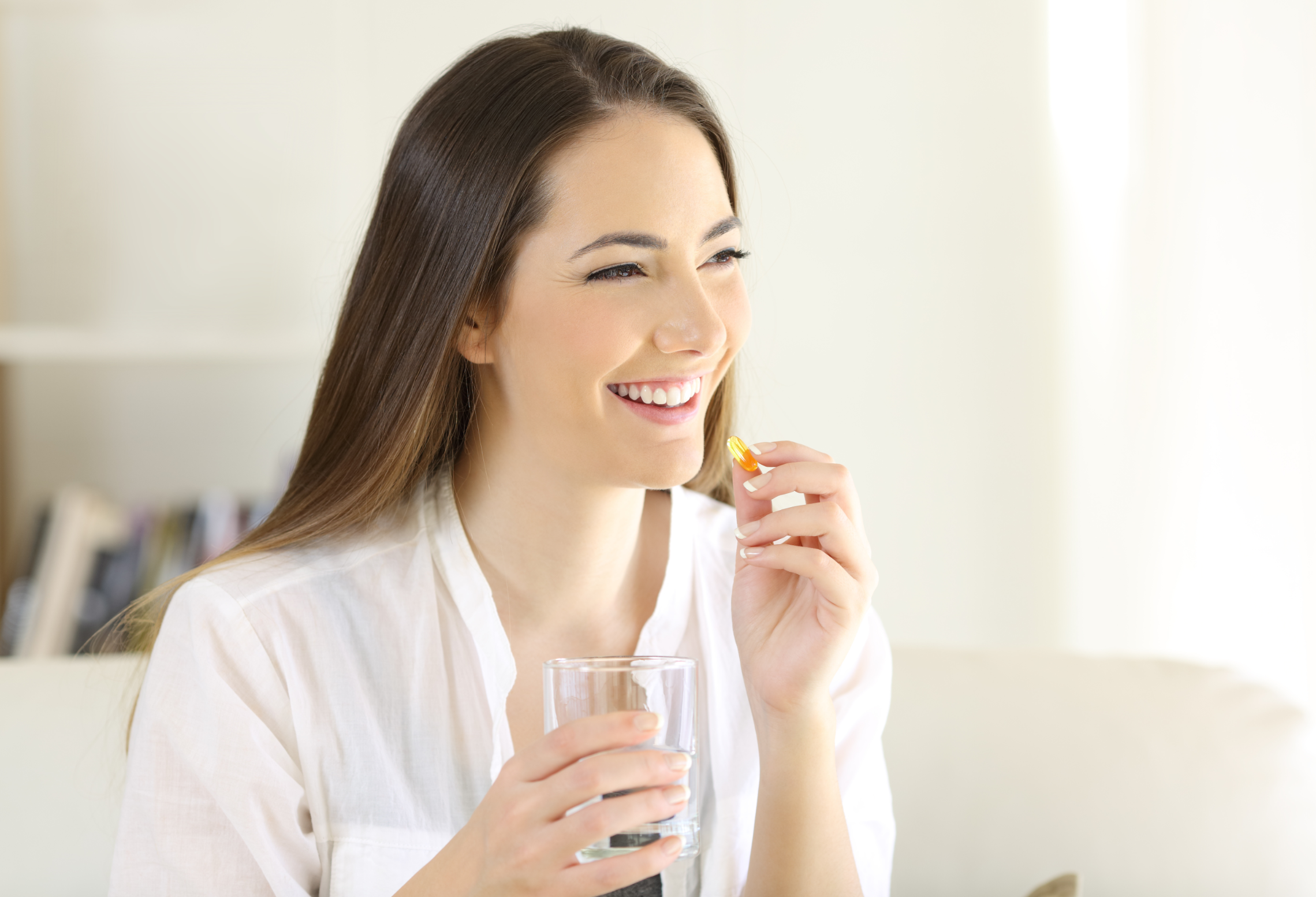 woman taking a vitamin yellow pill sitting on a couch in the living room at home