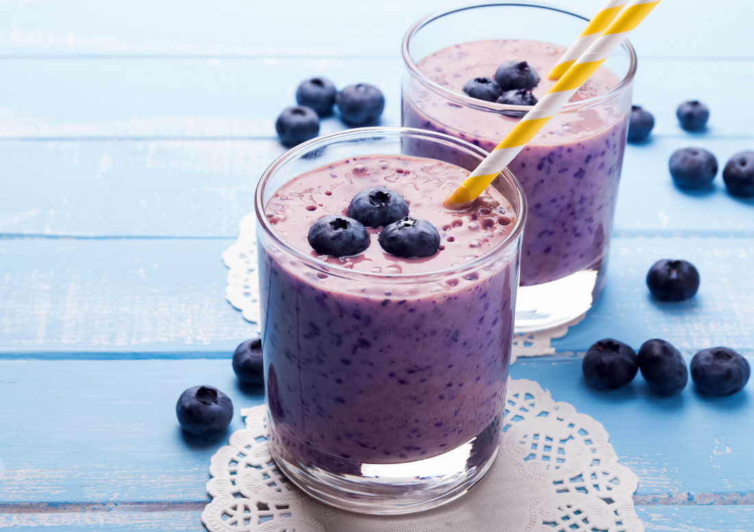 Two glasses of blueberry smoothie on blue colored wooden table