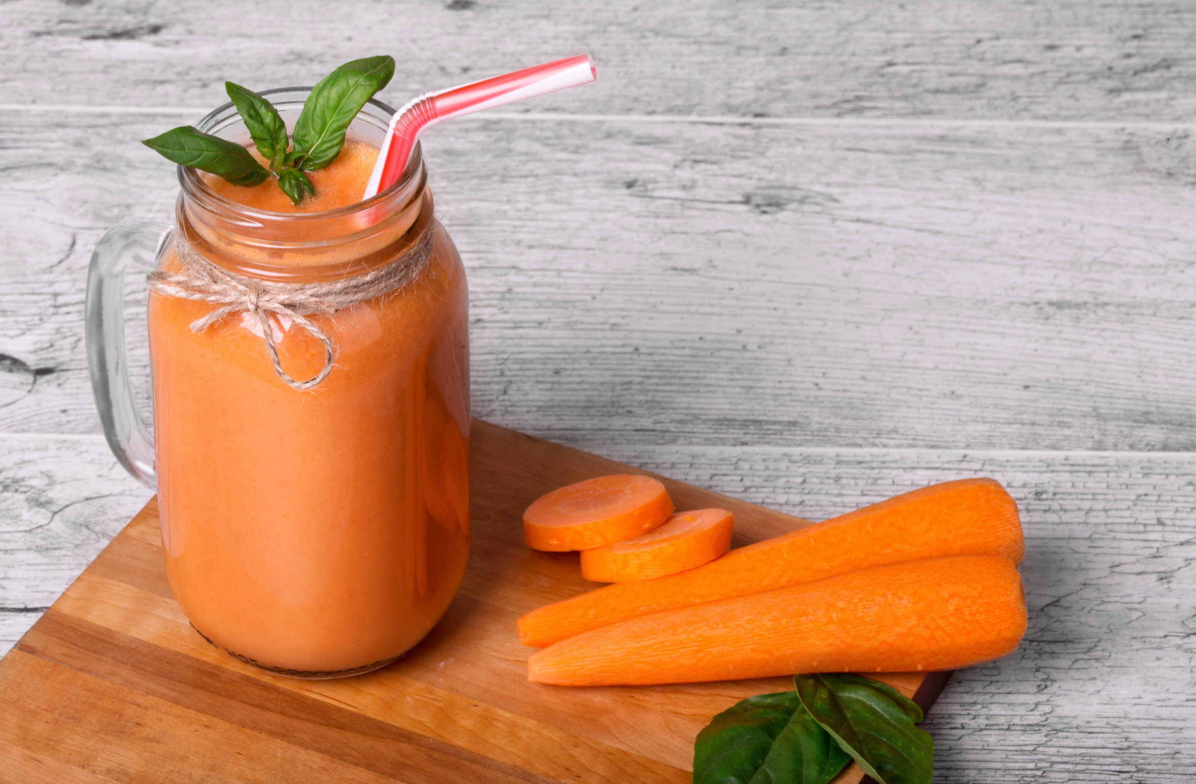 carrot smoothie with decorative basil leaves on a gray wooden background