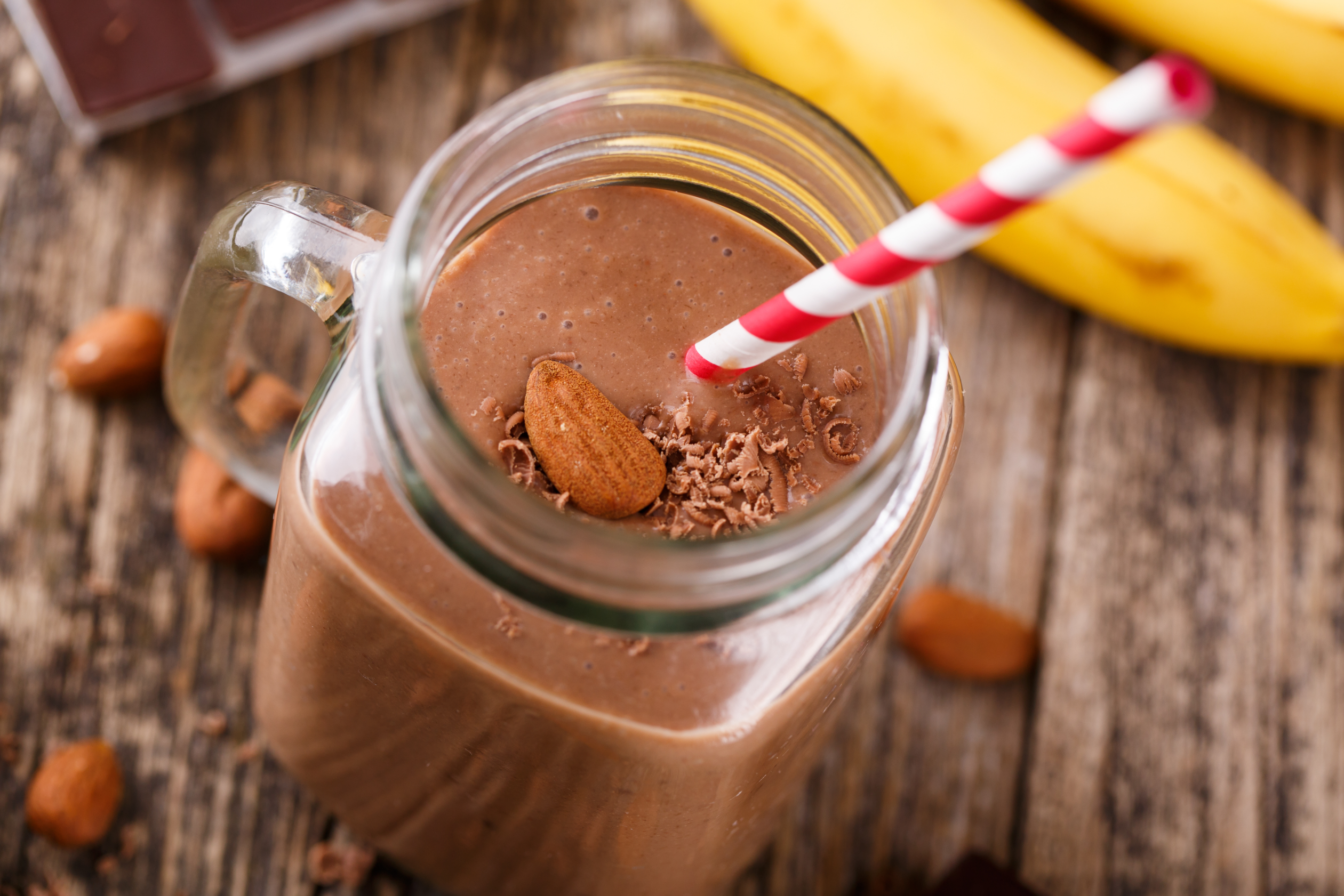 chocolate smoothie in glass jar with nuts and chocolate pieces on table