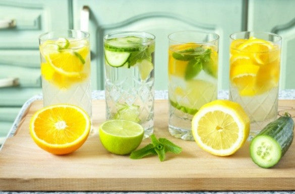four glasses of water with sliced lemon, cucumber, lime and orange