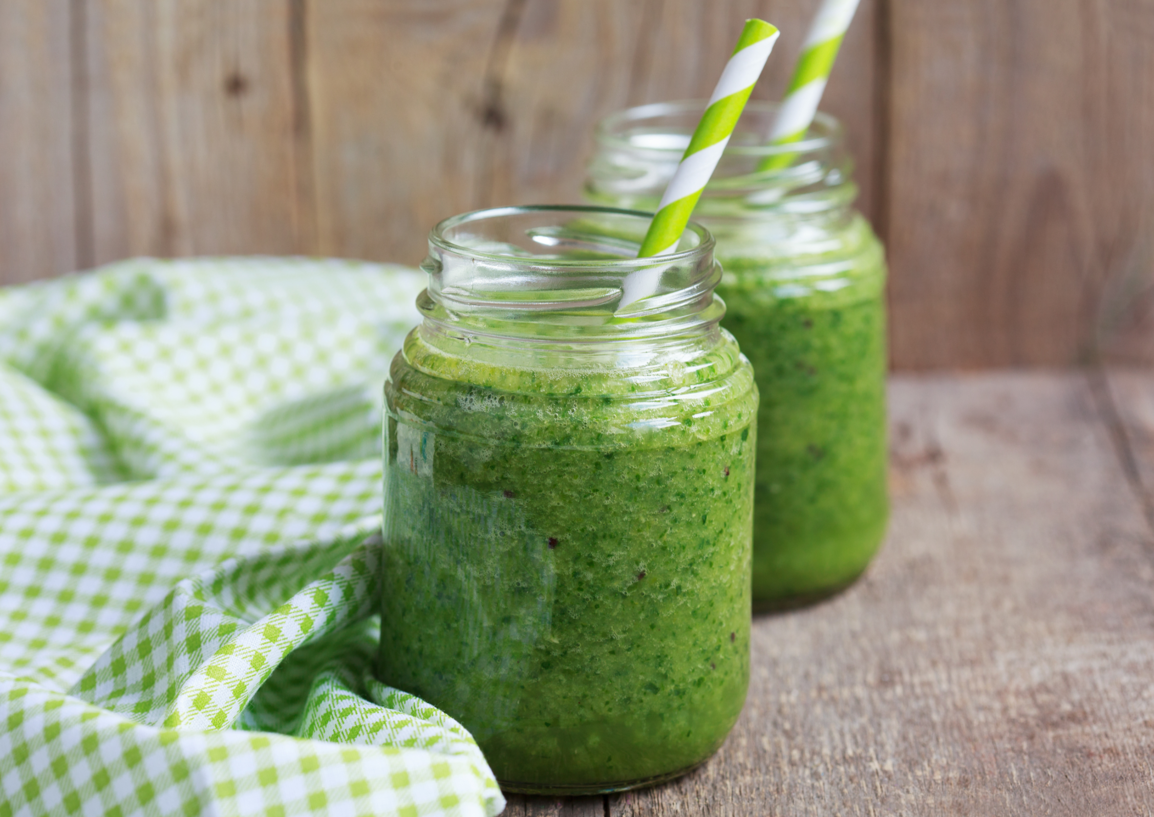 green smoothies in mason jars with straws on wooden background