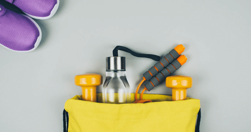 young woman happily weight lifting at gym. 310 nutrition's list of gym bag essentials will help you achieve your fitness goals.