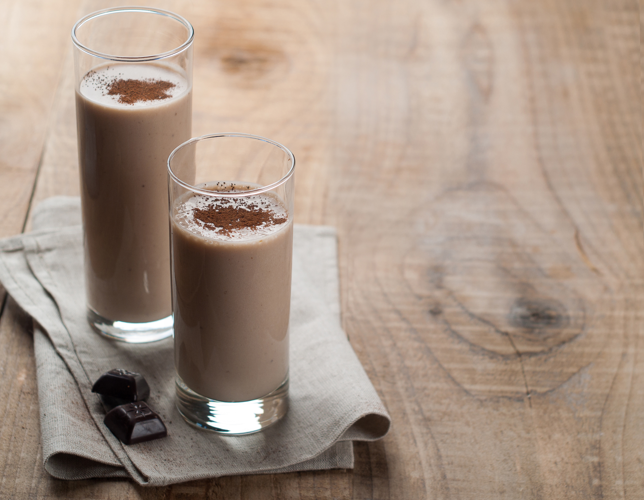 two tall glasses of cocoa almond shake on a wooden surface