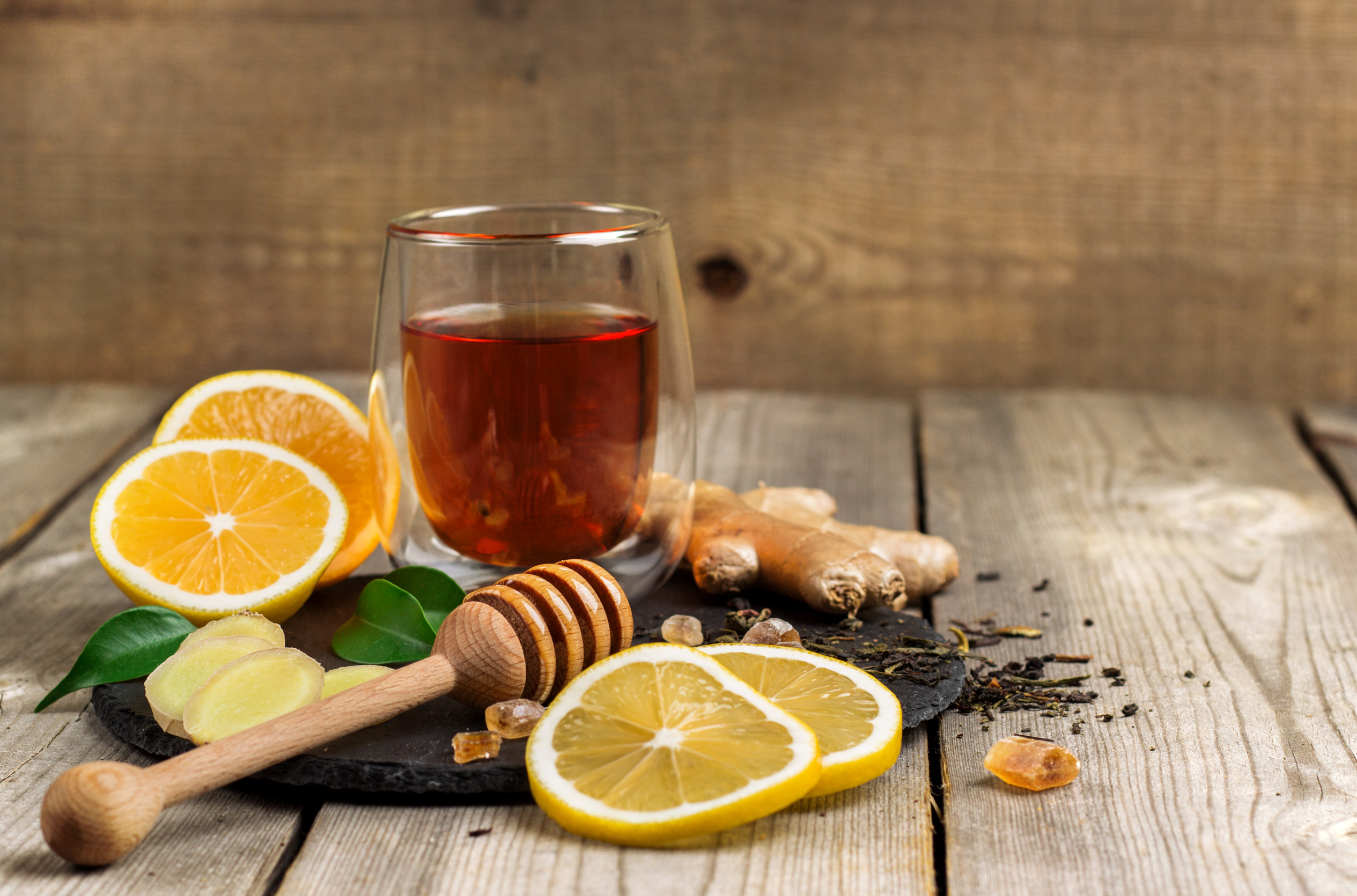 medicine ball tea glass surrounded by sliced lemon, ginger and mint leaves