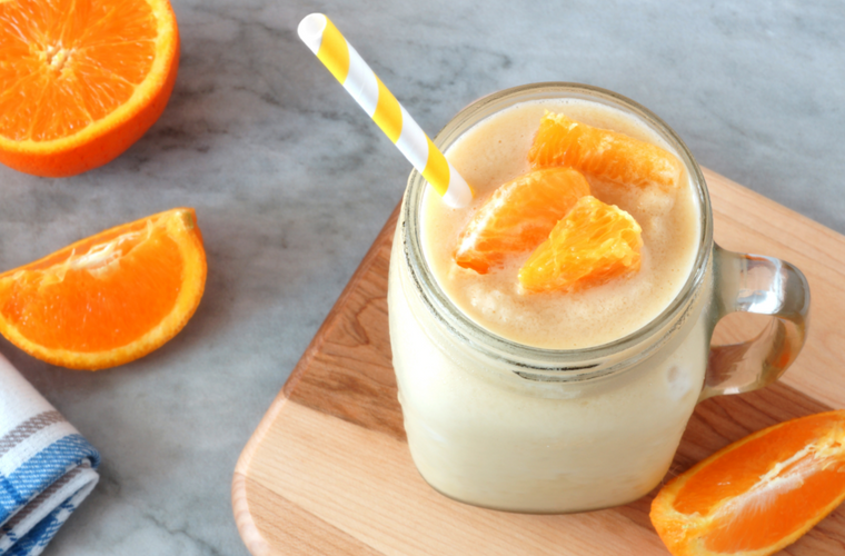 smoothie in a mason jar glass with straw resting on wood with fresh orange slices