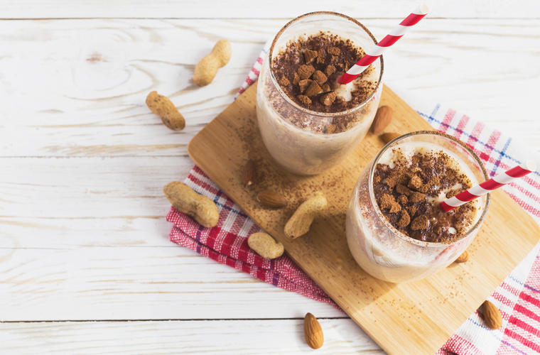 Overhead view of two glasses of peanut butter s'mores shake and whole peanuts on a wooden surface