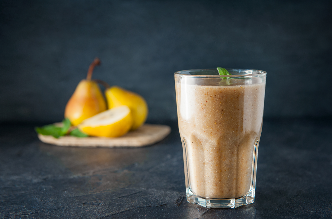 a glass of pear apple protein smoothie and fresh pears at the background