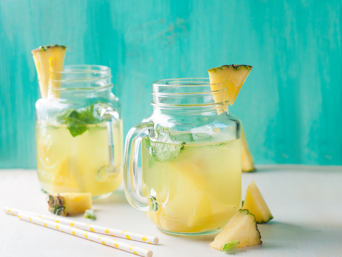 two mason jars of pineapple mango lemonade garnished with sliced pineapple and mint leaves