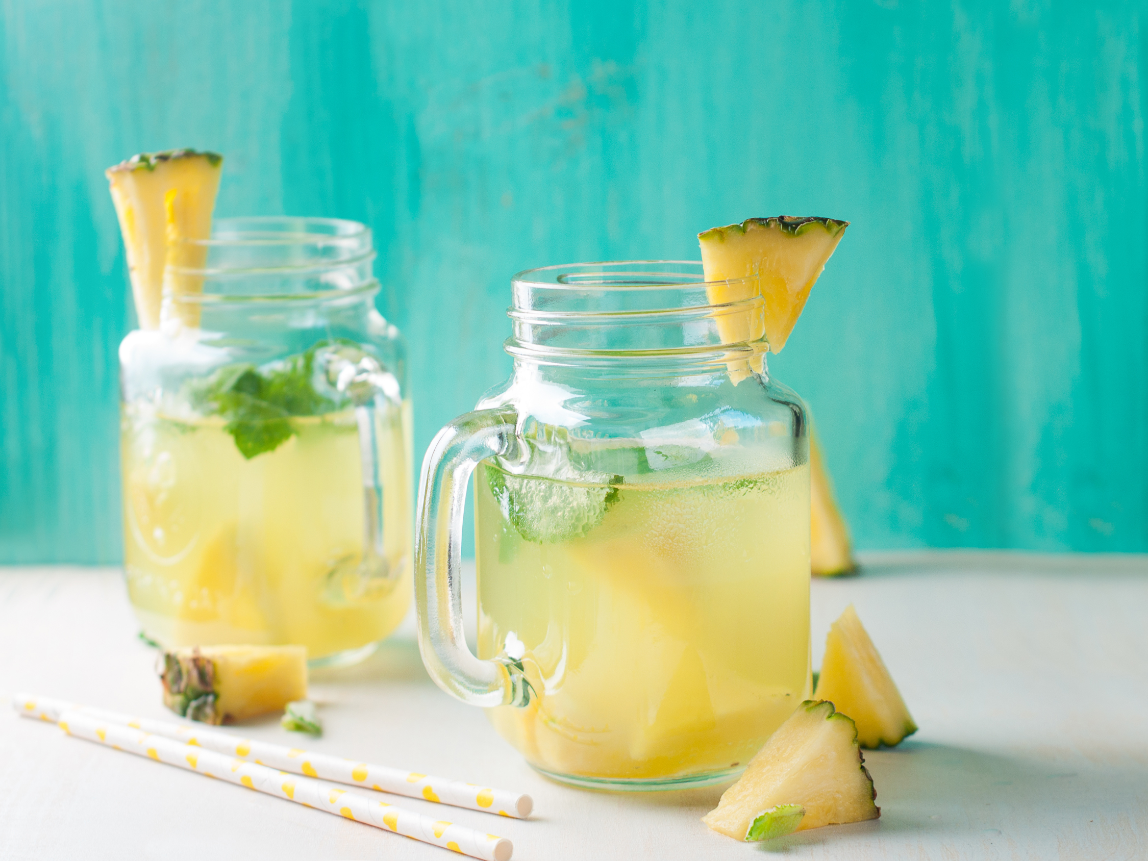 two mason jars of pineapple mango lemonade garnished with sliced pineapple and mint leaves