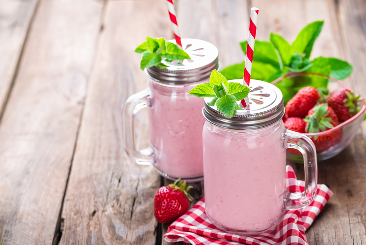 two mason jar of pink coconut smoothie and a bowl of fresh berries