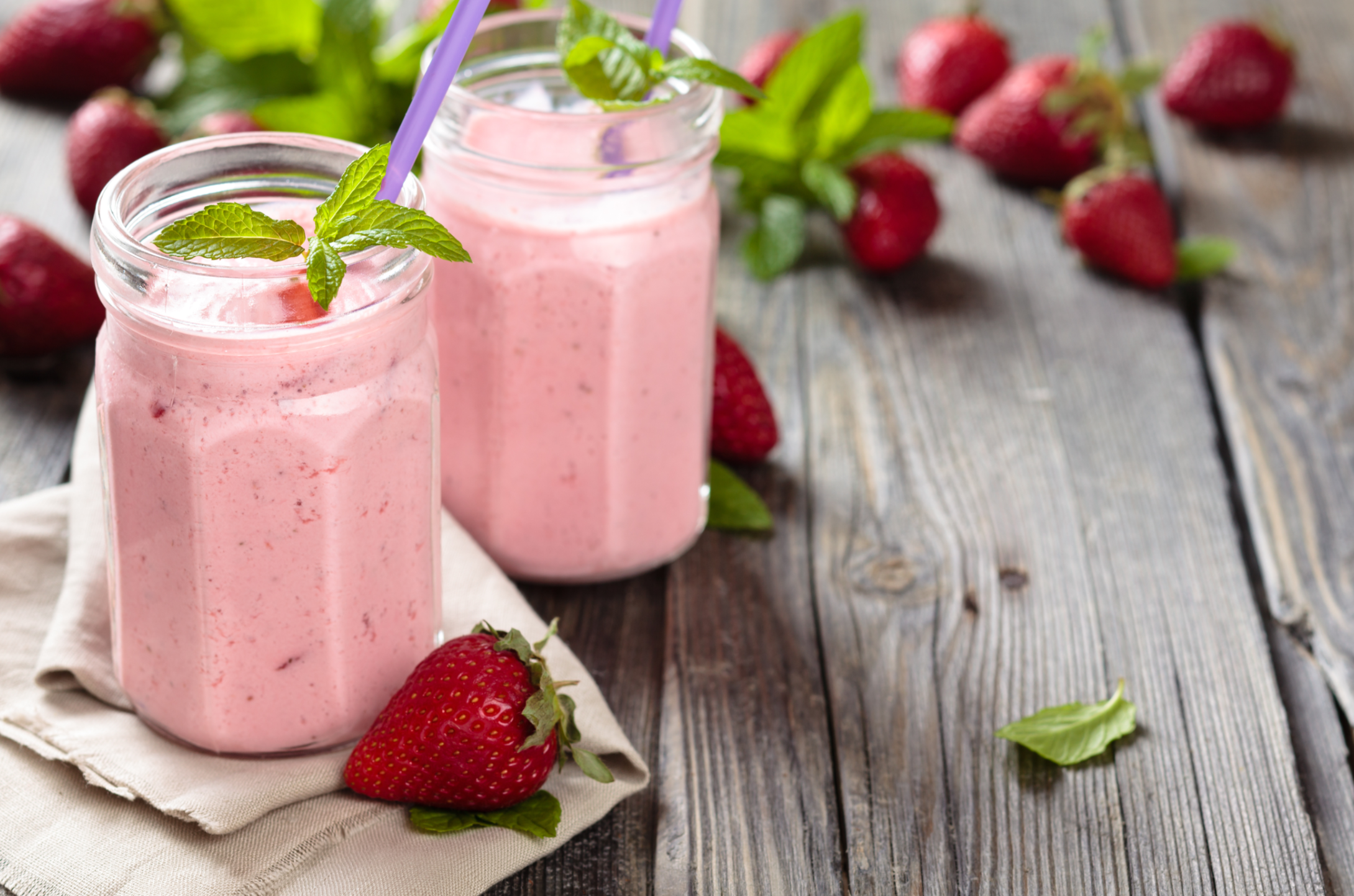 two glasses of strawberry jelly shake and fresh strawberries on a wooden surface