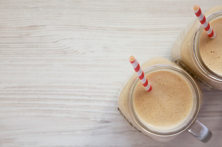almond butter keto smoothie in glass jars on a white wooden background, overhead view