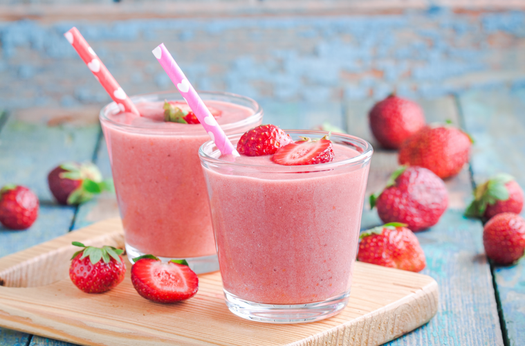 Two glasses of strawberry smoothie with straws on a wooden board