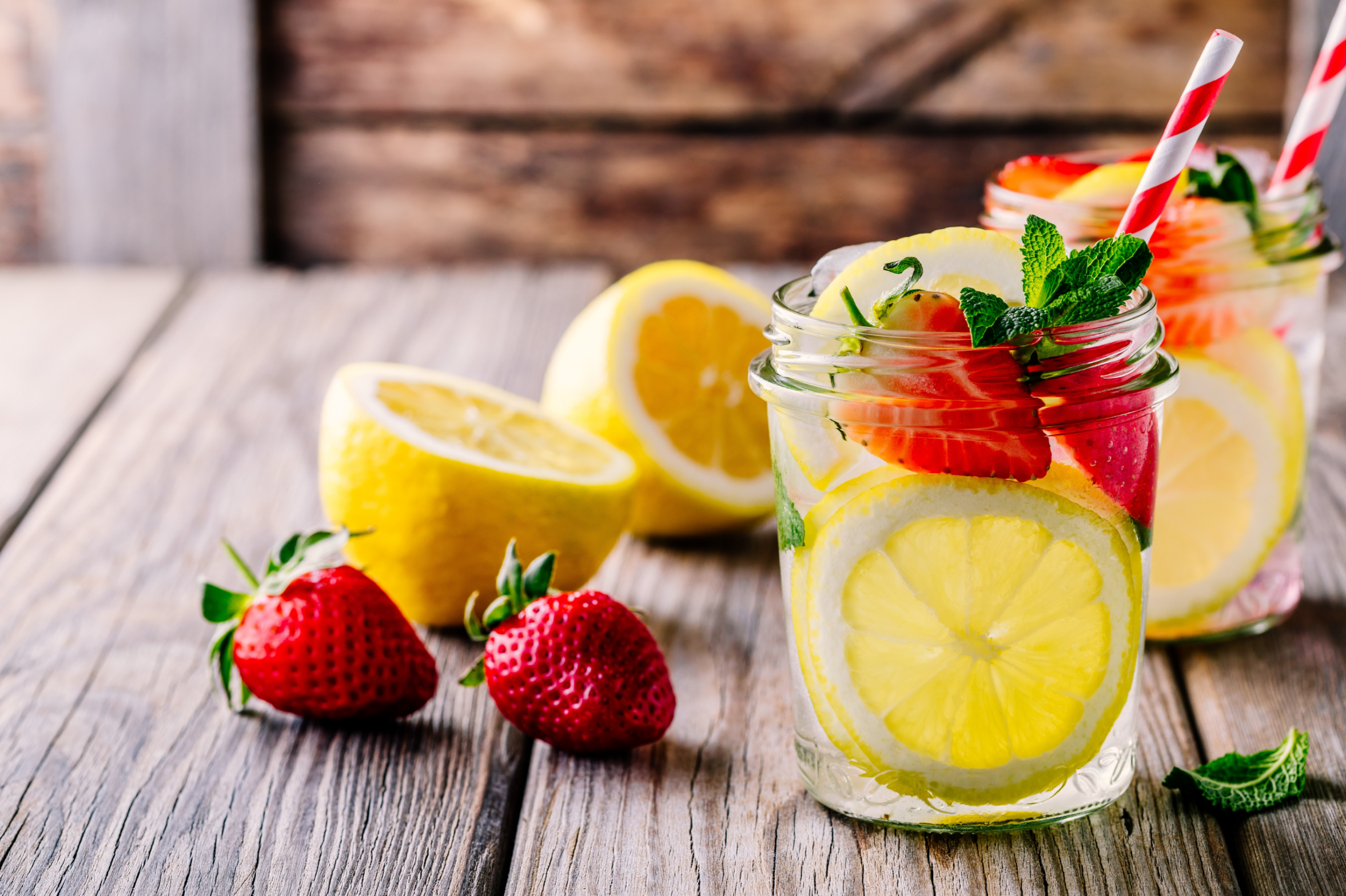 Lemon and strawberry lemonade in glass mason jars on a wooden background