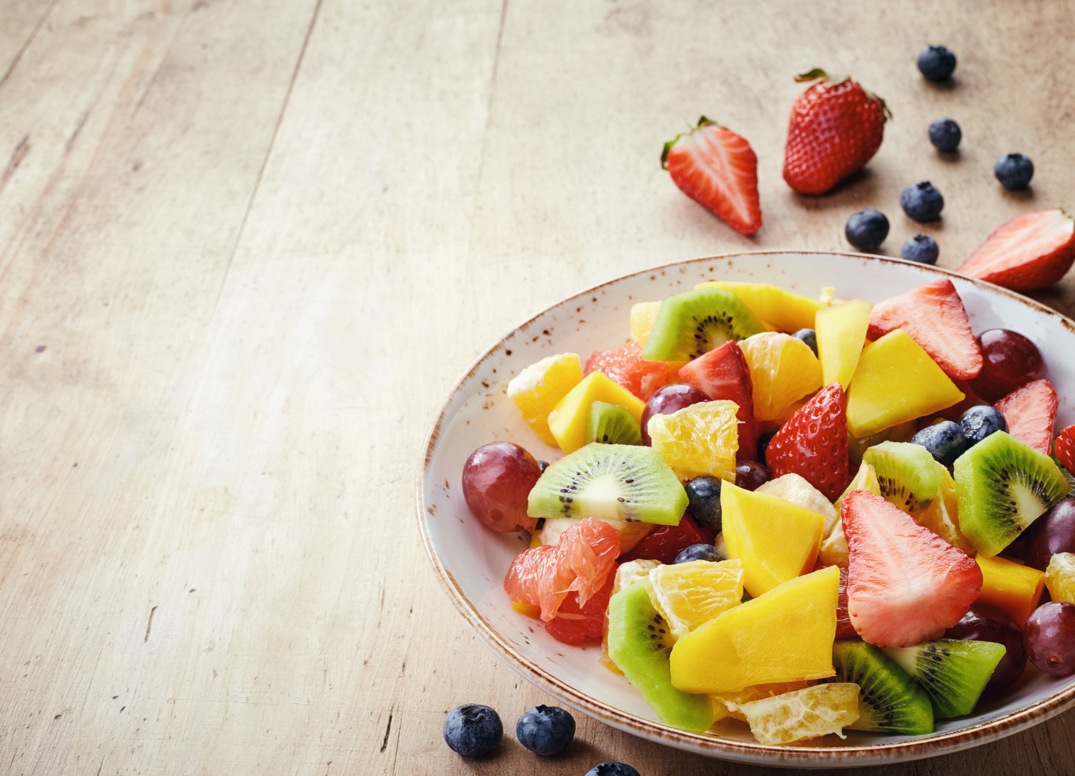 Bowl of healthy fresh fruit salad on wooden background