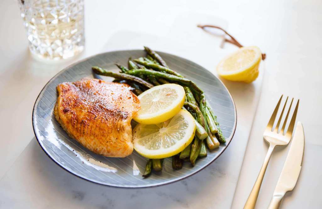 Baked tilapia fish with asparagus on a ceramic plate