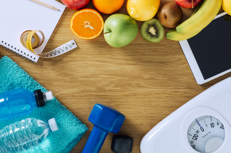 Fitness and weight loss concept, dumbbells, white scale, towels, fruit, tape measure and digital tablet on a wooden table, top view