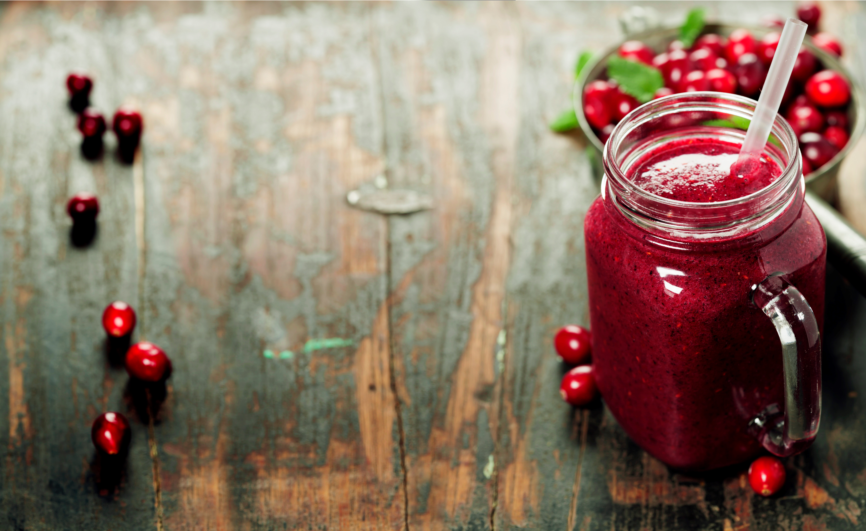 winter berry smoothie in a mason jar and a bowl of fresh berries in a wooden surface
