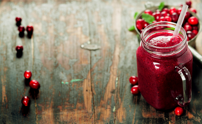 winter berry smoothie in a mason jar and a bowl of fresh berries in a wooden surface